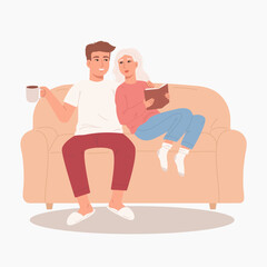 Couple sitting on the sofa. Family evening on sofa with book and cup of hot beverage. Lovers pending time together.
