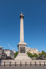 Fototapeta premium London, UK- July 4, 2022: Trafalgar Square. East side of Nelson's Column against blue sky showing High Commission of Canada with its flag in the back. Crane on horizon. Some green foliage