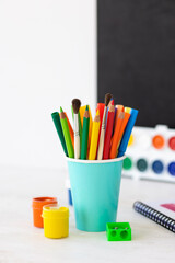 Time to return back to school. Bright colourful green yellow, blue stationery, paints, pencils, markers, brushes. black board on background. White alarm clock. Copy space for text. Autumn, September