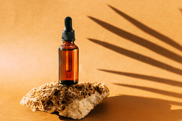 Cosmetic dropper bottle stone podium pedestal. Brown background with hard shadows from plant branch