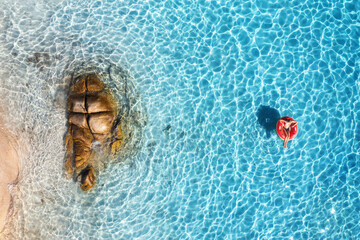 Aerial view of a young woman swimming with red swim ring in blue sea at sunset in summer. Tropical...