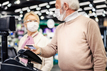 A senior couple at self-service cash register paying with credit card during corona virus.