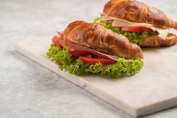 two lye croissant sandwiches with iberian ham, tomato slices, lettuce and cheese on marble board on...