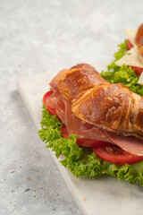 two lye croissant sandwiches with iberian ham, tomato slices, lettuce and cheese on marble board on grey background
