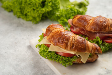 two lye croissant sandwiches with iberian ham, tomato slices, lettuce and cheese on marble board on...