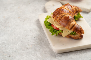 two lye croissant sandwiches with iberian ham, tomato slices, lettuce and cheese on marble board on...