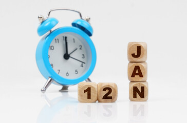 Wooden cube calendar for January 12, next to a blue alarm clock.