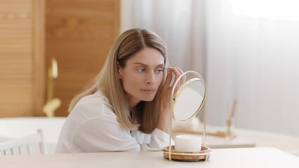 Domestic grooming concept. Beautiful middle aged woman wearing silk bathrobe plucking eyebrows herself, empty space - Powered by Adobe