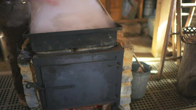 Sugar shack house with wood fire pan and iron kettle evaporator concentrating and evaporating steam for production of maple syrup in Highland country, Virginia