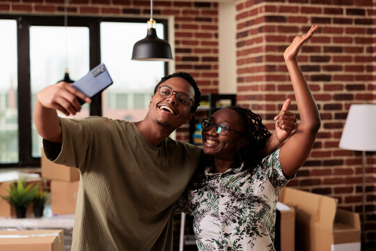 Positive husband and wife taking pictures and recording video in new house, filming apartment relocation after moving in. Using smartphone app to capture life event and home property.