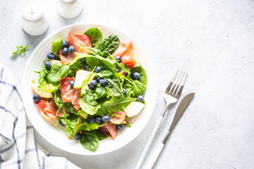 Healthy salad with spinach, jamon, pear and blueberry. Top view on white background with space for text.