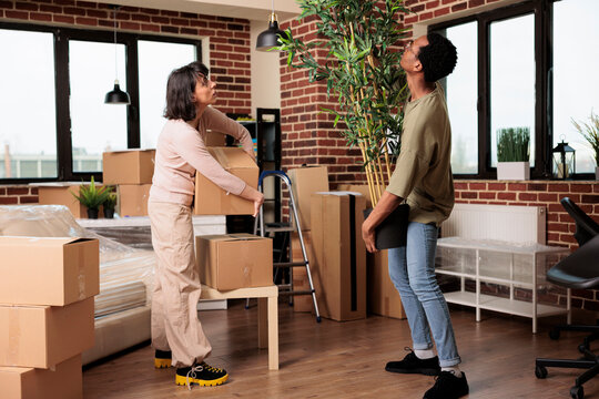 Diverse couple buying first home and moving in together, unpacking plant and furniture to decorate new household. Enjoying property relocation with decor to start new lifestyle beginnings.