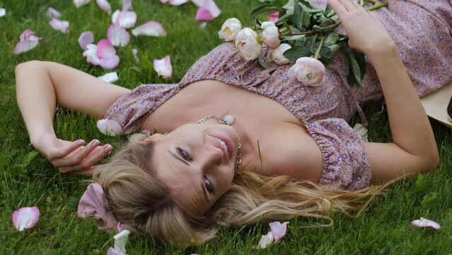 photographer takes pictures of a girl lying a beautiful woman in a green meadow, who holds a bouquet of peonies in front of her face in summer in nature