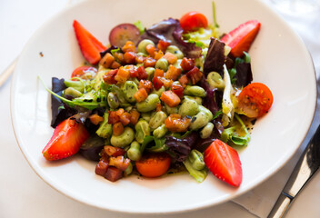 Colorful salad with candied beans, bacon marinated in soy-honey sauce, tomatoes, fruits and greens..