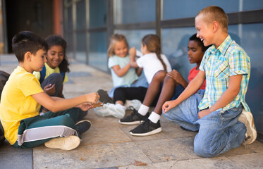 Smiling friendly preteen schoolmates funning outside near school during break between lessons in sunny spring day.