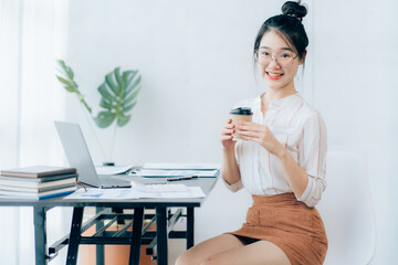 Portraits of beautiful smiling Asian women relax using laptop computer technology while sitting on their desks and using their creativity to work