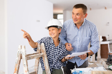 Adult man and preteen boy holding documents and talking in new house, planning design projects