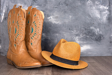 Leather cowgirl boots with a pattern and a hat stand on the floor against a gray wall.