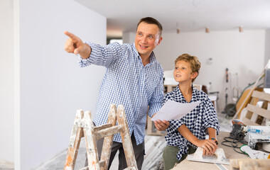 Adult man and preteen boy holding documents and talking in new house, planning design projects