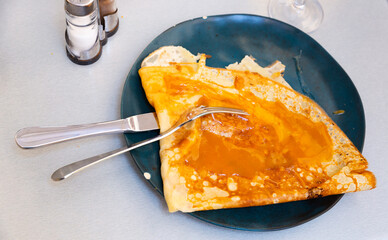 Just cooked crepe with salted butter caramel served on plate with serving pieces.