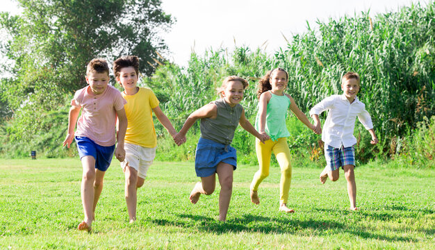 Group of school children, boys and girls, laughing and running in a city park at summer day