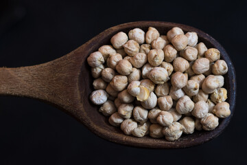 garbanzos crudos en cuchara grande de madera, sobre fondo negro