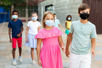 Boy and girl with in masks walking hand in hand together through town. Their friends walking behind them.