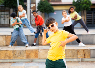 Obraz premium Confident tween boy hip hop dancer posing while performing with group on summer city street.