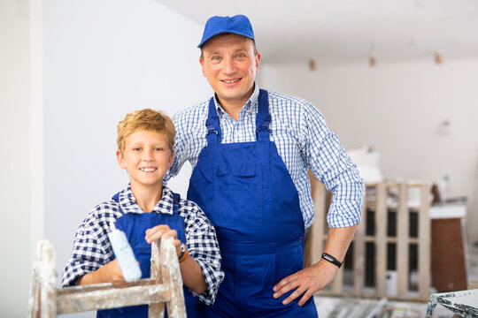 Portrait Of A Father And Little Son In Blue Overalls Painting The Walls In The Room