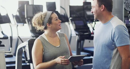 Personal trainer or coach talking to a client about managing his exercise schedule on a tablet. A happy female fitness instructor consulting a fit man about this workout performance at the gym
