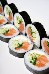 Sushi on a white background in sesame seeds with avocado and nigiri. Futomaki with salmon and cucumber. Food.