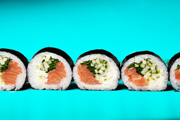 Sushi on a green blue background in sesame with avocado and nigiri. Futomaki with salmon and cucumber. Food.