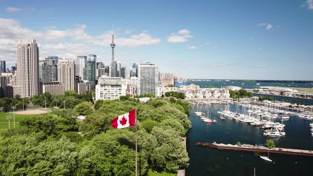 Aerial Footage of the Toronto Skyline on a bright summer day. The camera orbits around a Canadian Flag in the foreground with the CN tower in the background.