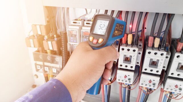 an electrician is using a thermogun to analyze sub-wires and components, use digital infrared thermometer to find out overcurrent loads, and abnormalities in the panel's electrical system.