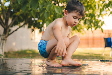 Child having fun playing with water in the yard. Happy family. Summer holidays. Sunny day.