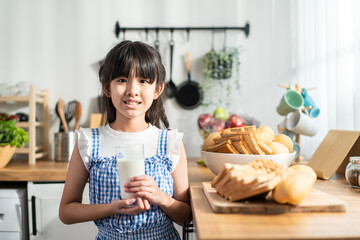 Asian little kid holding a cup of milk and drinking in kitchen at home