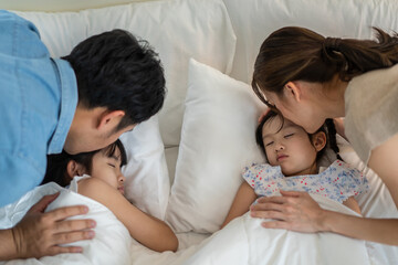 Asian loving parents take care of sleeping daughter in bedroom at home