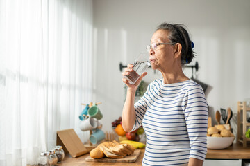 Asian senior mature woman drinking a glass of milk in kitchen at home. 