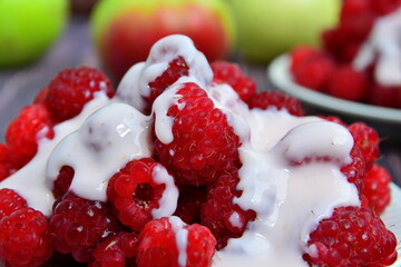 Berries still-life. Heap of red ripe juicy fresh sweet raspberries filled with milk cream or yogurt close up on apples background. Selective focus
