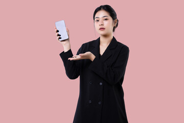 Young modern business asian woman holding smartphone mobile device and showing blank screen display isolated over pink background.