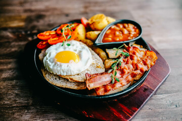Delicious English breakfast with a fries egg, beans, bacon, and roasted potatoes.
