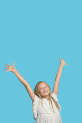 Childhood happiness. Smiling young girl rise her hands up to the sky. Happy kids. Looking to camera isolated. Blue background.