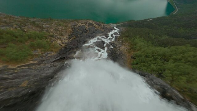 Aerial fpv flight downhill Langfoss Waterfall flowing into idyllic lake of Norway