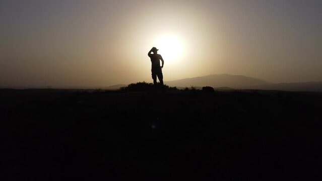 Silhouette of a man with fedora hat on sunset on tumulus hill.