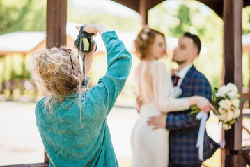 A wedding photographer photographs a couple in nature on a sunny day - obrazy, fototapety, plakaty