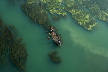 Fishermen are seen floating on top of algae as they search for potential catch in the sharp green...