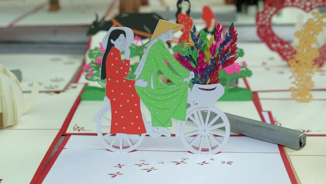 A stationary footage of a cycling couple paper craft with added flowers design on their bicycle's basket. This was shot in Hội An, a city in Vietnam.