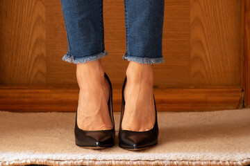 Women's legs in jeans and black high-heeled shoes on the floor of the house on the carpet near the door, women's shoes with heels, shoes