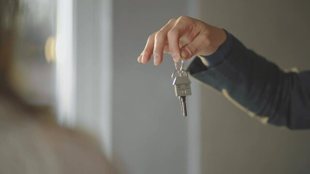 Male hand holding key with house shaped keyring and giving it to woman. Moving into new apartment concept.