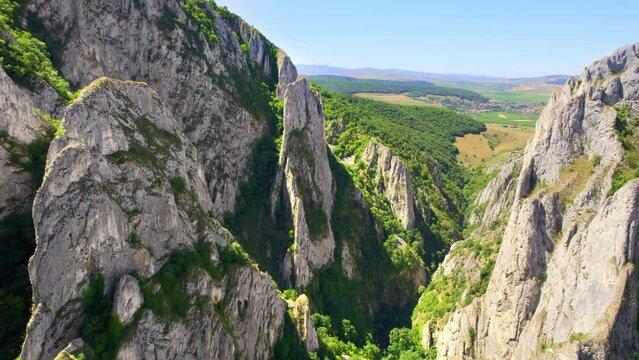 Aerial drone view of a rocky canyon in Romania. Rocky cliffs with sparce vegetation. Fields in the distance